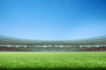Low-angle view of a vibrant green grass field inside a large, empty sports stadium under a clear blue sky