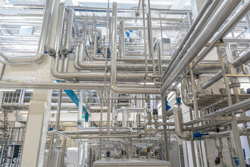 Modern industrial factory interior with stainless steel pipes and processing machinery. Clean automated production line in food, dairy, or chemical plant engineering industry.