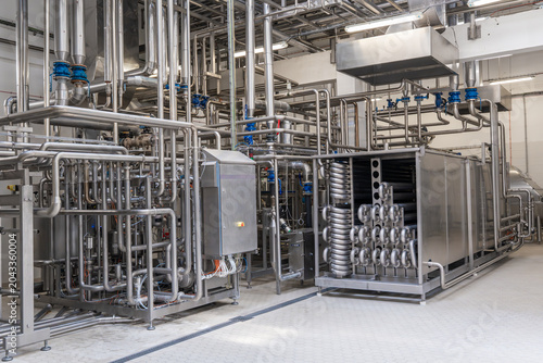 Modern industrial factory interior with stainless steel pipes and processing machinery. Clean automated production line in food, dairy, or chemical plant engineering industry.