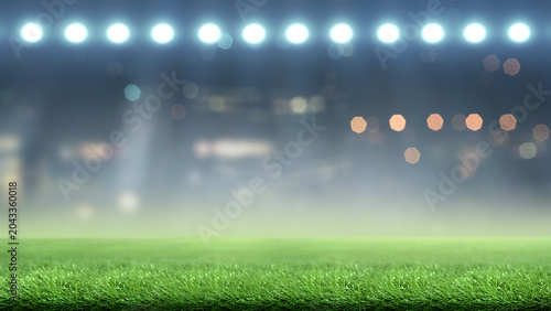 Blurred stadium background with bright floodlights shining on green grass turf at night