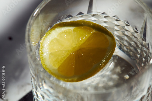 Top view of a fresh lemon slice in a textured glass of water. Healthy hydration and detox drink concept.