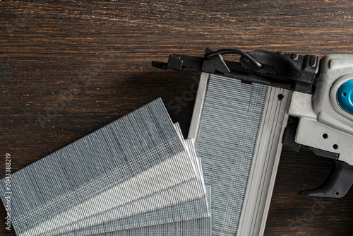 Konstfotografi Brad nailer gun with collated brad nails on wooden background, closeup