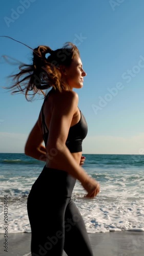 Athletic woman jogging along the beach. Vertical video.