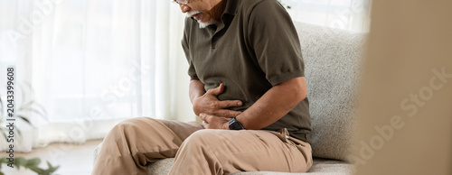 Abdominal pain stomach ache senior man stomach pain belly pain healthcare digestive problem home living room sofa Senior man sitting sofa living room holding abdomen with abdominal pain