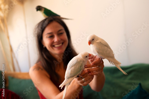 Cuadro en lienzo Young woman playing with her pet parakeets at home
