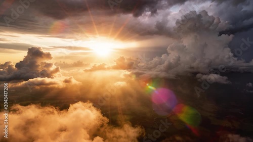 Flying over a panoramic sunset cloudscape, a beautiful aerial timelapse of animated cumulus clouds drifting as the golden sun breaks through with peaceful god rays, set against a dramatic stormy sky.