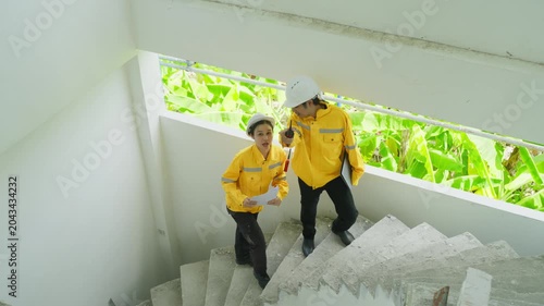 Construction worker stair inspection safety yellow jacket indoor workwear helmet concrete stairway site visit building interior handrail maintenance architecture team climbing stairs