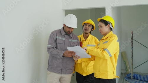 Construction worker group reviewing plan unfinished interior room, safety helmet site inspection, project planning document discussion, teamwork renovation job site, hardhat interior inspection