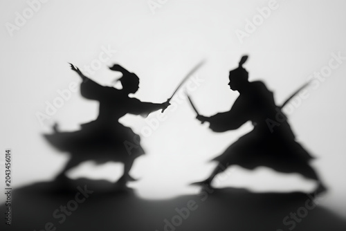 Dynamic black & white shadow play depicting two traditional warriors in a fierce sword duel with motion blur, creating an artistic and dramatic combat scene.