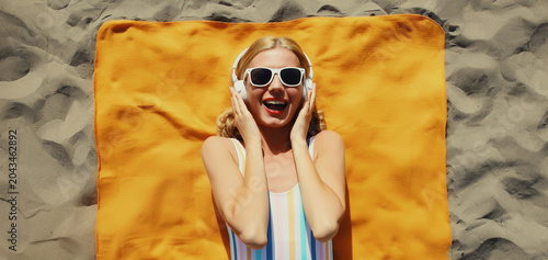 Summer vacation, happy cheerful woman listening to music lying on the beach, relaxed girl on towel