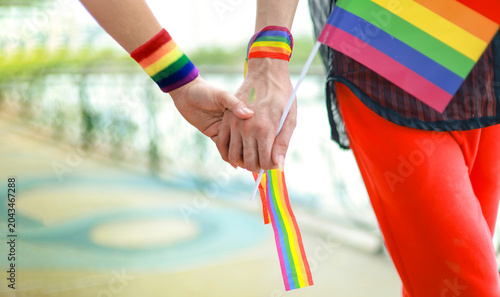 Fotografie Gay couple's hands clasped together wrists tied pride flag representing love sexual attraction other men LGBTQ as they walk hand in hand displaying affection park during parade supporting equality