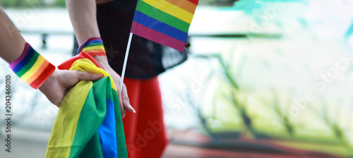 Gay couple's hands clasped together wrists tied pride flag representing love sexual attraction other men LGBTQ as they walk hand in hand displaying affection park during parade supporting equality.
