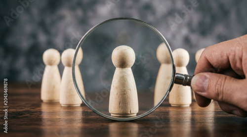 Magnifying glass focusing on wooden figure, human resources recruitment concept, talent search and candidate selection process