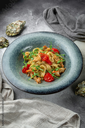Restaurant style seafood tagliatelle with shrimp, cherry tomatoes and fresh microgreens served on a blue ceramic plate with oyster shells