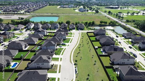 Greenbelt residential divide in Arlington, TX highlights two parallel rows of homes separated by landscaped corridor with young trees open lawn. Visible ponds distant rooftops in upscale area