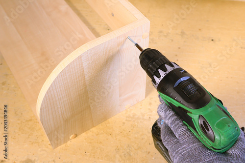 Person using green cordless drill to screw into curved wooden panel