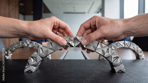 Human hands connecting intricate metallic puzzle pieces to form a curved geometric structure