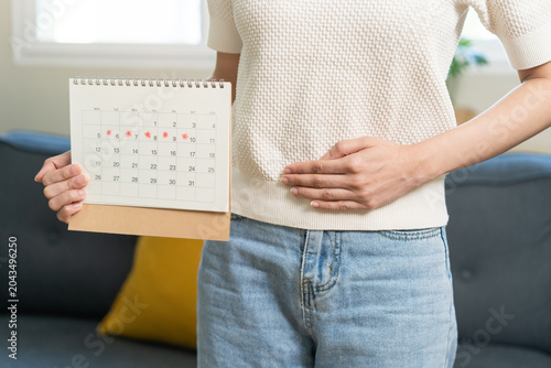 Menstruation, periods cycle day of monthly, hurt young woman, girl stomachache, hand holding marking symbol on calendar for missed and delay or late at home. Medical, healthcare, gynecological concept
