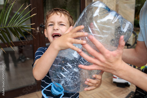 Foto Little boy in navy striped shirt grabs a large plastic water bottle with both ha