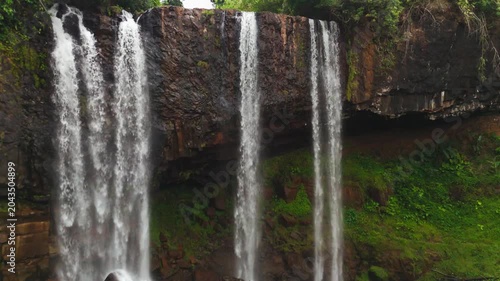 Drone video of Tad Tayicseua Waterfall dropping through lush green jungle in Attapeu Province, Laos. The powerful cascade tumbles over rocky ledges surrounded by dense tropical vegetation. This remote