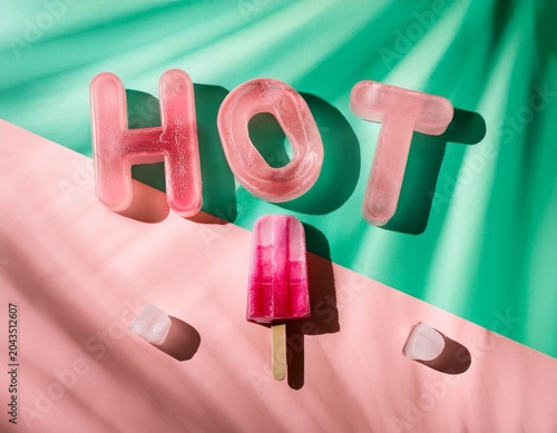 Top view of HOT 3D letters made with ice on pale green mint and pink tie and dye background with pink popsicles and copy space