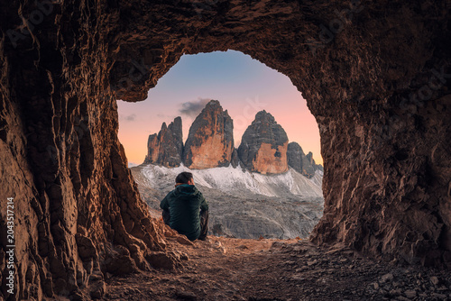 Foto Male tourist admiring the Tre Cime Peak from rocky cave during evening in Dolomi