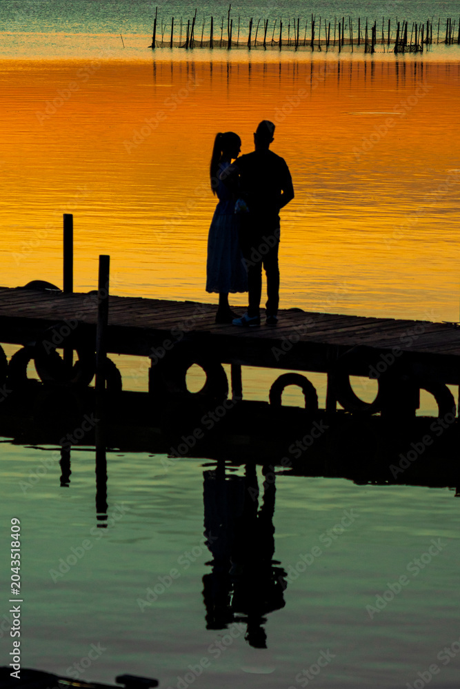 Obraz premium honeymoon. vacation. silhouette of a couple in love on a wooden pier, enjoying a sunset on a lake