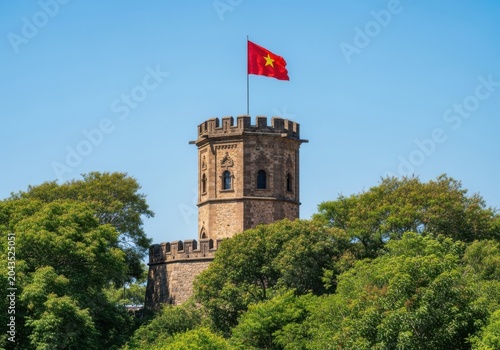 Ancient stone tower with a red flag featuring a yellow star flying on top, surrounded by lush green trees