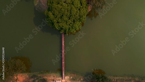 Photography Wooden bridge connecting earth to a green island tree, top down aerial view