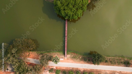 Photos Overhead view of a walkway extending across a serene lake to a lush green tree