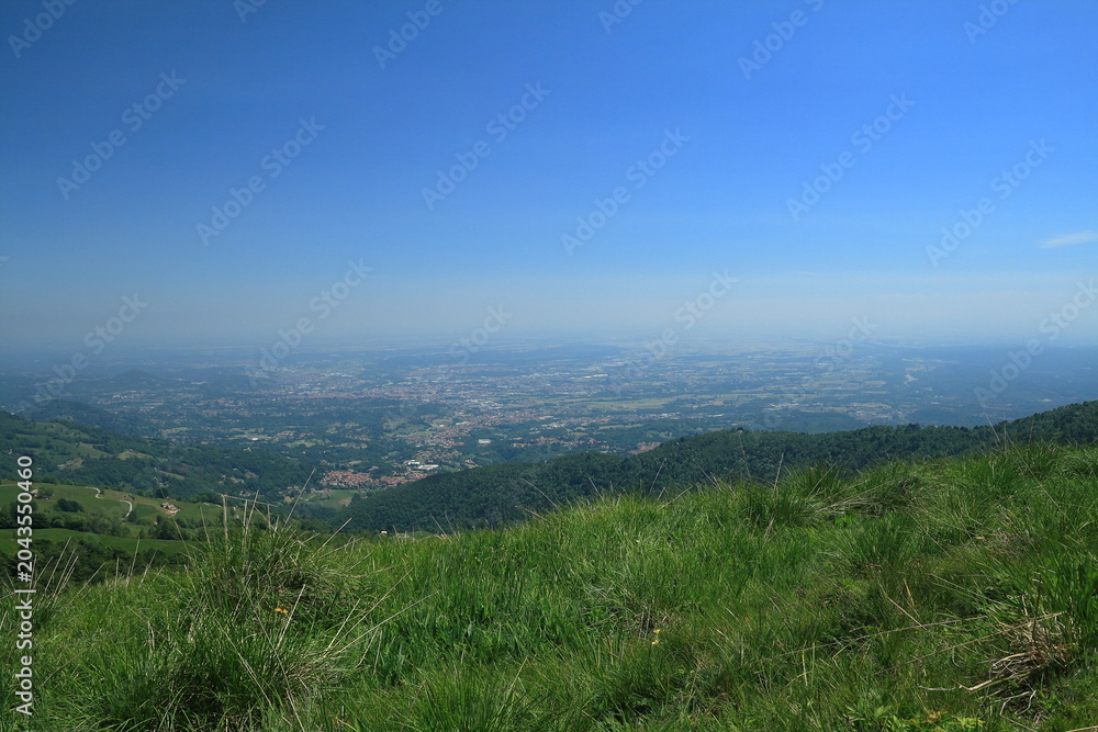 Fototapeta premium Panoramic view of a vast valley and distant plain from a green mountain hill under a clear blue sky