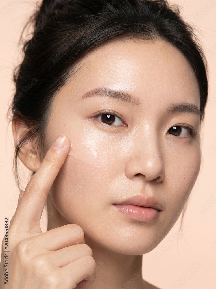 Obraz premium Young Asian woman applying clear gel serum to cheek for skin care