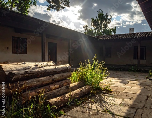 Rustic Courtyard with Stacked Wooden Logs in Sunlit Old House Exterior