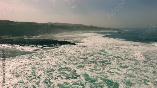 Aerial drone view with at the camera passing in and passing by a fisherman on the rocks at the beach.