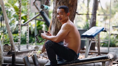 Photos Asian man exercising at outdoor street gym, building strength with improvised eq