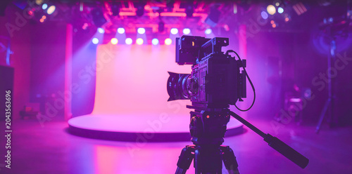 Professional cinema camera on tripod in neon television studio