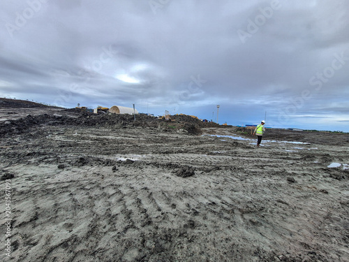 Industrial construction site with muddy tire-tracked ground and vibrant blue and cloudy sky. Active construction or mining site. Selective focus.