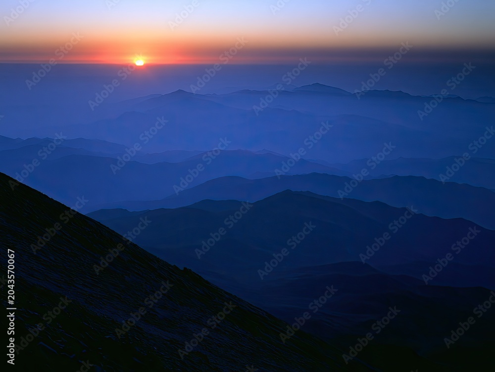 Fototapeta premium Misty, layered mountains fade into a soft, golden sunrise