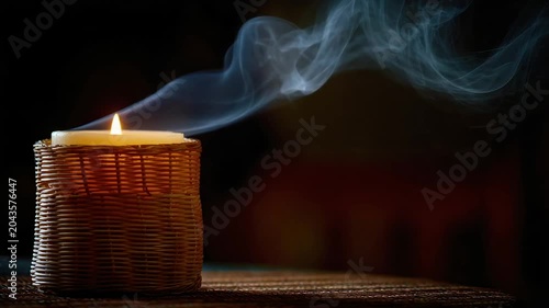 Lit candle in a woven basket with flowing smoke against a dark background