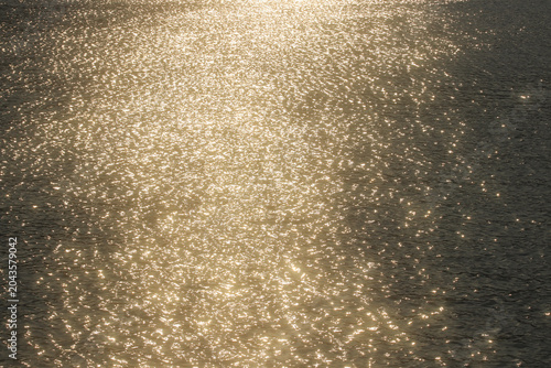 Tableau sur toile Golden sunlight reflections shimmer across rippling water, creating an elegant abstract nature background with sparkling highlights, warm tones and luxurious visual texture