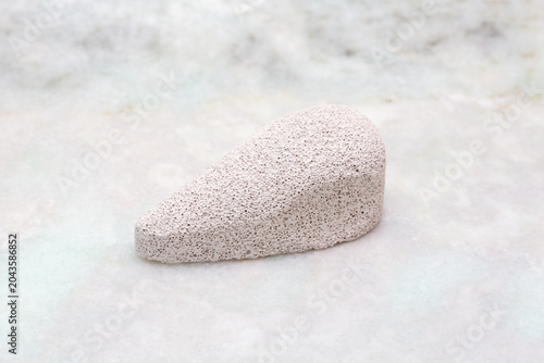 Pumice stone with a smooth surface and tapered shape, placed on a light marble background, showcasing its porous texture and natural color variations