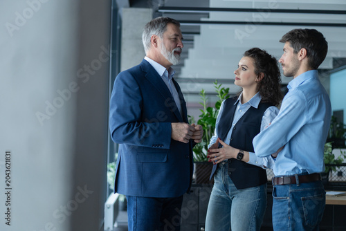 Three busy coworkers discussing project, standing in modern office