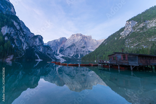 Schilderij op canvas Majestic mountain reflection on a calm alpine lake with wooden boathouse at dawn