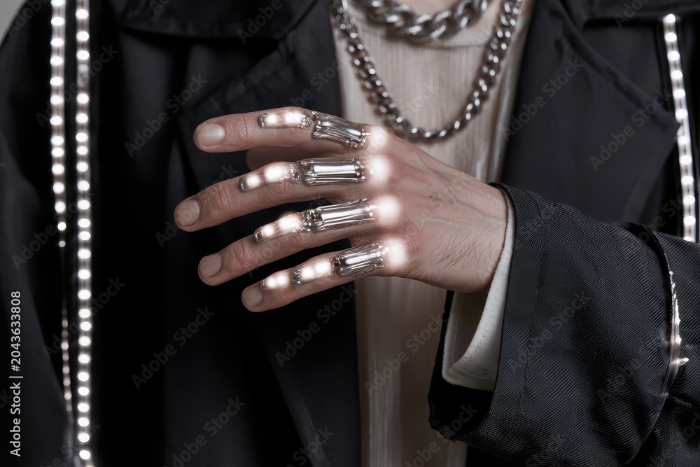 Naklejka premium Close-up of a person's hand adorned with futuristic glowing rings and a chunky silver chain necklace.