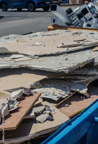 Broken drywall gypsum board and plaster debris piled in construction dumpster with scrap metal at demolition waste site outdoors