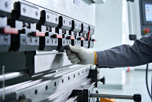 Foto Worker's gloved hand adjusts a metal press brake machine in a factory setting