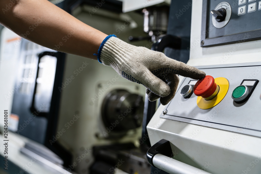 Obraz premium Worker's gloved hand presses the red emergency stop button on industrial machinery