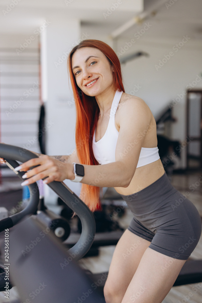 Fototapeta premium Athletic woman with red hair training on a treadmill in a fitness center, focusing on a healthy and active lifestyle