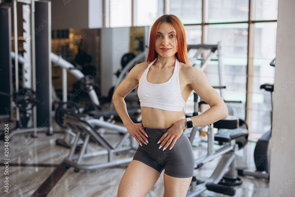 Fototapeta premium Fit healthy woman with red hair posing at a modern gym, embodying strength and wellbeing for an active lifestyle
