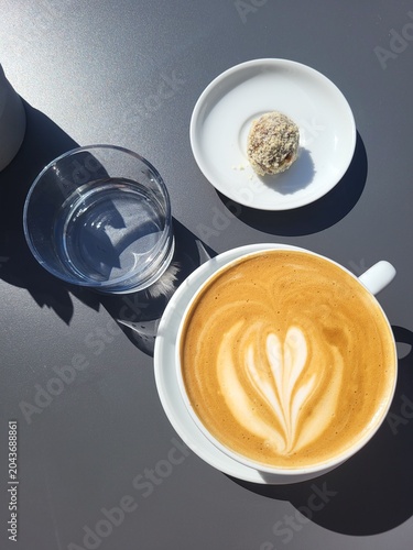A cup of cappuccino, a glass of water, and a healthy dessert on a black table.